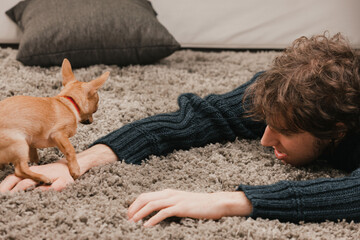 Young man relaxing on carpet with small dog