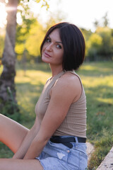 Portrait of a young pretty woman, sitting on a wooden stairs in green public park 