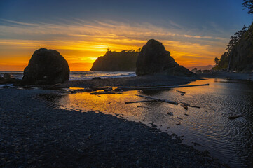 Colorful sunset at Ruby Beach featuring sea stacks silhouetted against the vibrant sky, with tide pools and driftwood on the pebble shoreline in Olympic National Park, Washington state, USA