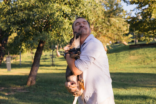 Smiling middle-aged man walks and plays with a small dog in public park