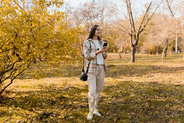 attractive young woman walking in autumn wearing jacket using phone