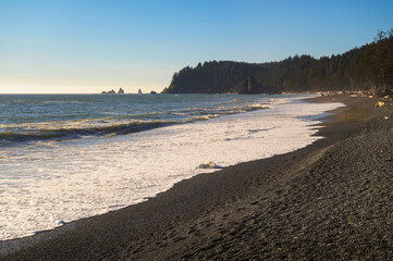 Pebble-covered Rialto Beach with forested headland and sea stacks in Washington State. Rialto Beach, situated within Olympic National Park, is located near La Push, the Quileute Tribe's residence.
