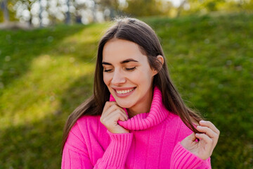 young smiling woman in pink sweater walking in green park