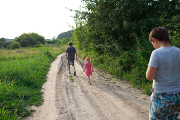 Children walking down a dirt road in a lush green landscape during the golden hour of late afternoon