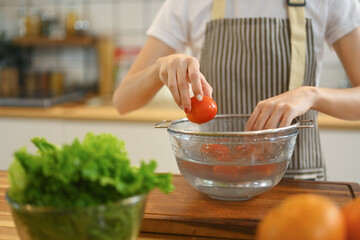 Close up shot of woman washing tomato while preparing healthy vegan salad in kitchen