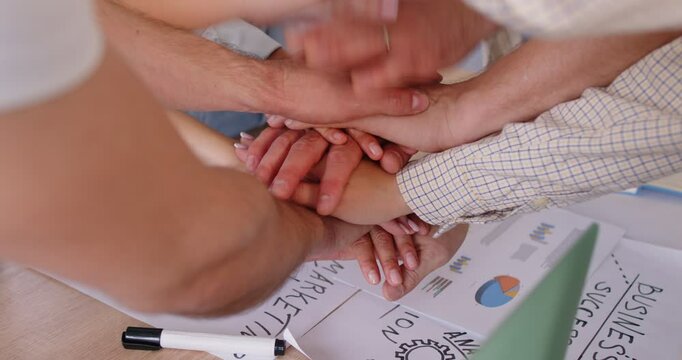 Business team working on marketing plan and stacking their hands. Group of creative people gather around table, discuss strategy ideas and pile up their hands. Teamwork, success, cooperation concept