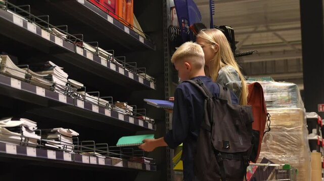 Brother and sister annoyed because has to choose new notebooks for the school. Unhappy kids shopping for the new school year. Sale for stationery items.
