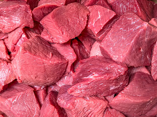 Obraz premium Food and eating concept, Raw meat with red bloody in the tray, Pile of chopped beef on pieces, Slices of uncooked cow meat on the table, Fresh recipe preparation for cooking.