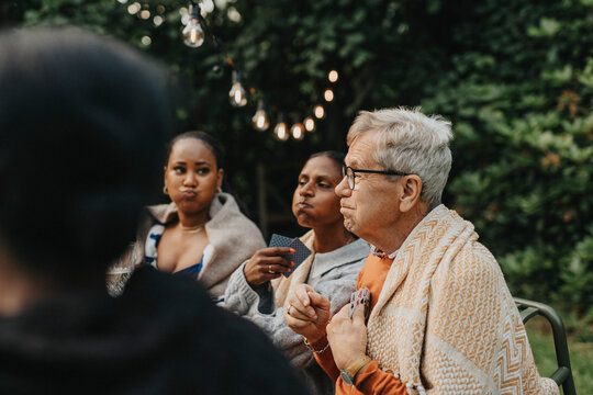 Senior man making face with family members and playing cards at garden party
