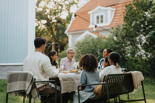 Male and female family members discussing and having lunch during social gathering at garden party