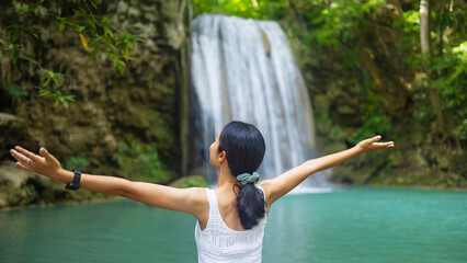 Woman traveler happy at deep forest waterfall. Erawan Waterfall National Park, Kanchanaburi, Thailand.