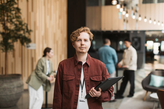 Portrait of young male delegate holding folder while standing at convention center