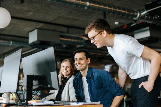 Smiling male and female computer programmers sharing computer screen in office