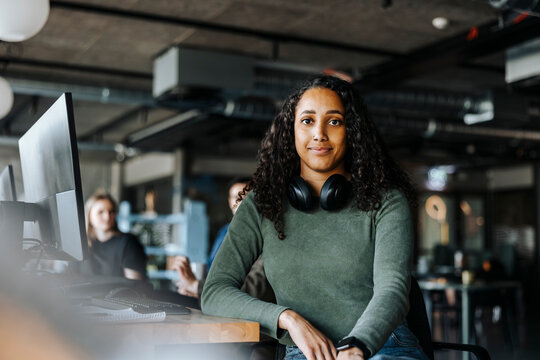 Portrait of young female tech entrepreneur with wireless headphones sitting in office