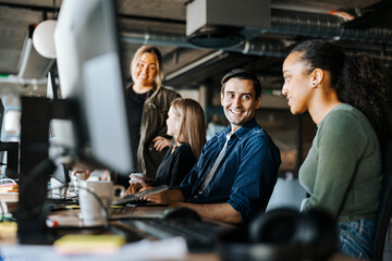 Happy male and female entrepreneurs discussing while sitting in tech startup office