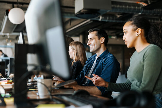 Female entrepreneur discussing with happy male colleague while working in tech startup office