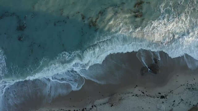 Aerial panning point of view shot looking down on waves crashing during sunset on the rocks of Lucy Vincent Beach in Martha's Vineyard, Massachusetts