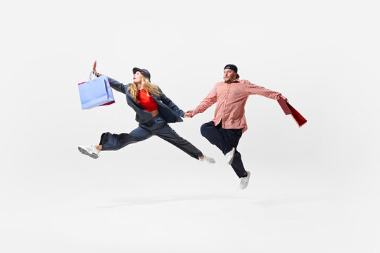 Running for sales. Energetic young couple in motion, running with colorful shopping bags. Thrill of sales, balancing shopping bags with acrobatic grace. Shopping, sales, Black Friday, fashion concept