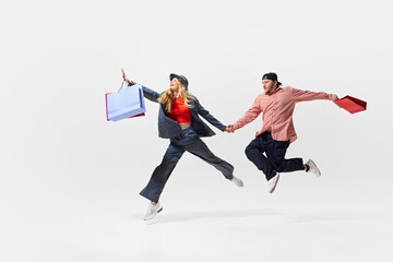 Running for sales. Energetic young couple in motion, running with shopping bags, Thrill of sales, balancing shopping bags with acrobatic grace. Shopping, sales, Black Friday, fashion, holiday concept