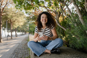 pretty curly woman walking in city street in striped t-shirt, using smart phone