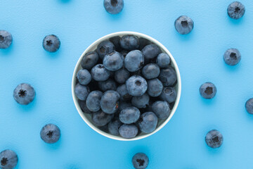 Fresh blueberries in white bowl on light blue table background. Pastel color. Healthy berries. Closeup. Top down view.