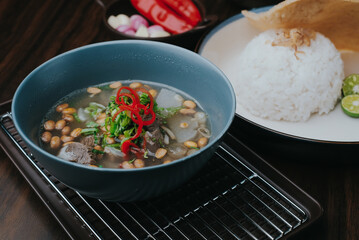 Soto or coto or soup Indonesian beef soup served with white rice, tomato, soy, and green onion. Side view om wooden background