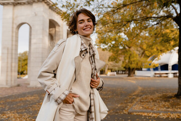 pretty smiling woman walking in park in autumn clothes
