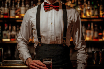 Fototapeta premium A dapper bartender, sporting a bow tie and suspenders, prepares a drink at a dimly lit bar, with bottles blurred in the background. 
