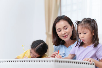 Asian mother supervising daughters sitting at table doing homework