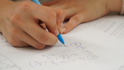High school teenagers in classroom, close up shot girl writing math exam, solving task on paper sheet. Modern education concept.