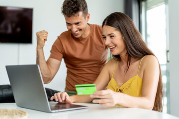 Excited couple celebrating successful online purchase.