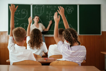 With hands up. Pupils, kids in the classroom together