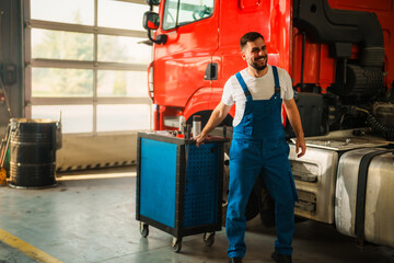 A satisfy mechanic pulling a blue tool cart in maintenance garage.