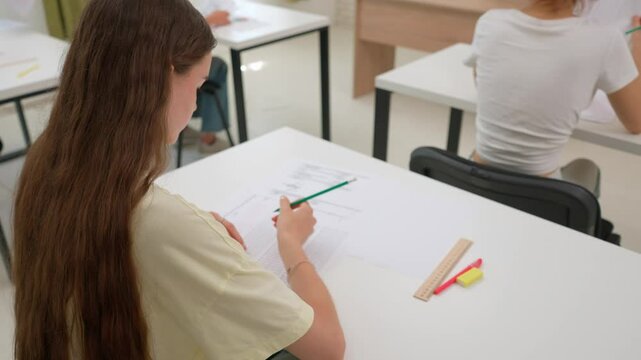 High school teenagers in classroom sitting at desks doing test, writing exam answering questions, joking during test. Modern education concept.