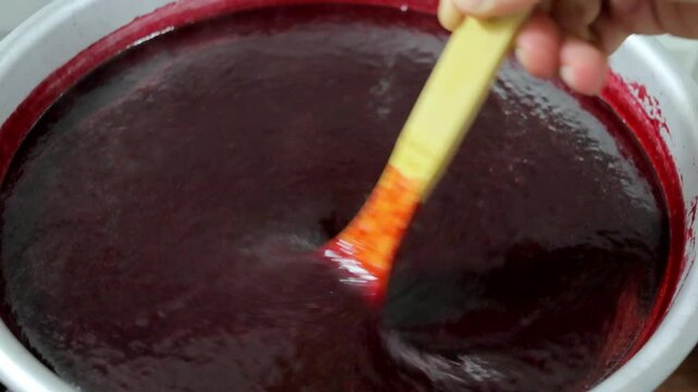 a man cooks plum jam in an aluminum basin, stirring it with a wooden spoon 4k video