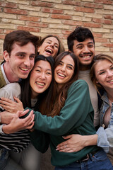 Vertical. Cheerful group of diverse young friends enjoying having fun together with brick wall in...