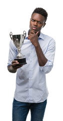 Young african american man holding trophy serious face thinking about question, very confused idea
