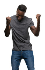 Fototapeta premium Young african american man wearing grey t-shirt very happy and excited doing winner gesture with arms raised, smiling and screaming for success. Celebration concept.