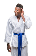 Young african american man over isolated background wearing kimono smiling with hand over ear listening an hearing to rumor or gossip. Deafness concept.