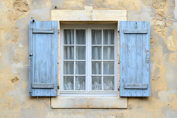 Fototapeta premium A Glimpse of Tranquility: Blue Shutters Frame a Charming Window with Delicate Lace Curtains, Adding a Touch of European Charm to a Weathered Wall.