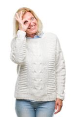 Middle age blonde woman wearing winter sweater over isolated background doing ok gesture with hand smiling, eye looking through fingers with happy face.