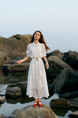 Woman in white dress embracing the ocean breeze on rocky shoreline