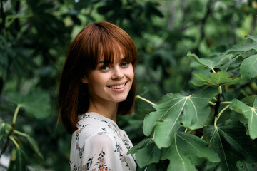 Beautiful redhead woman standing gracefully in front of vibrant green tree