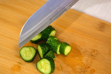 Woman cutting cucumbers pickles on wooden board to serve on kitchen at home, hands close-up....