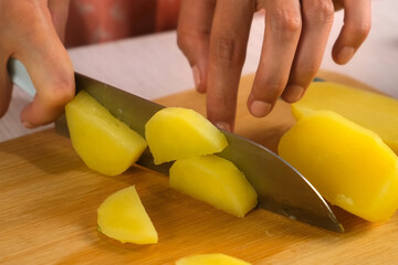 Woman cutting boiled potato on table cutting wooden board on kitchen at home, hands close-up....
