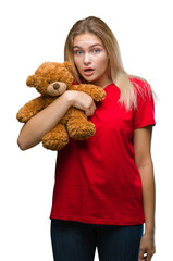 Young caucasian woman holding cute teddy bear over isolated background scared in shock with a surprise face, afraid and excited with fear expression