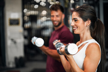 An athletic young adult woman lifting dumbbells with her boyfriend at the gym