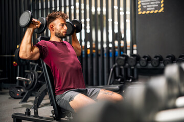 A fit young adult man using dumbbells for his exercises at the gym
