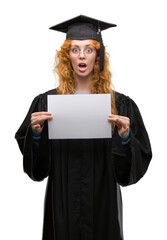 Young redhead woman wearing graduate uniform holding degree scared in shock with a surprise face, afraid and excited with fear expression