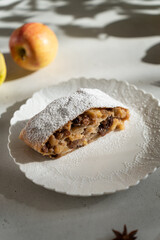 Apple pie - strudel or Apfelstrudel, sliced pie with apples, raisin and cinnamon on a gray table. Traditional German or Austrian pastry. Homemade apple strudel with fresh apples and powdered sugar.